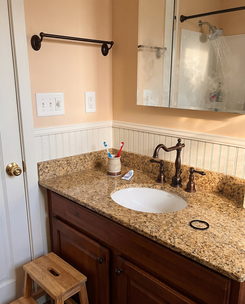 A family bathroom vanity with kids' toothbrushes and the shower running in the mirror